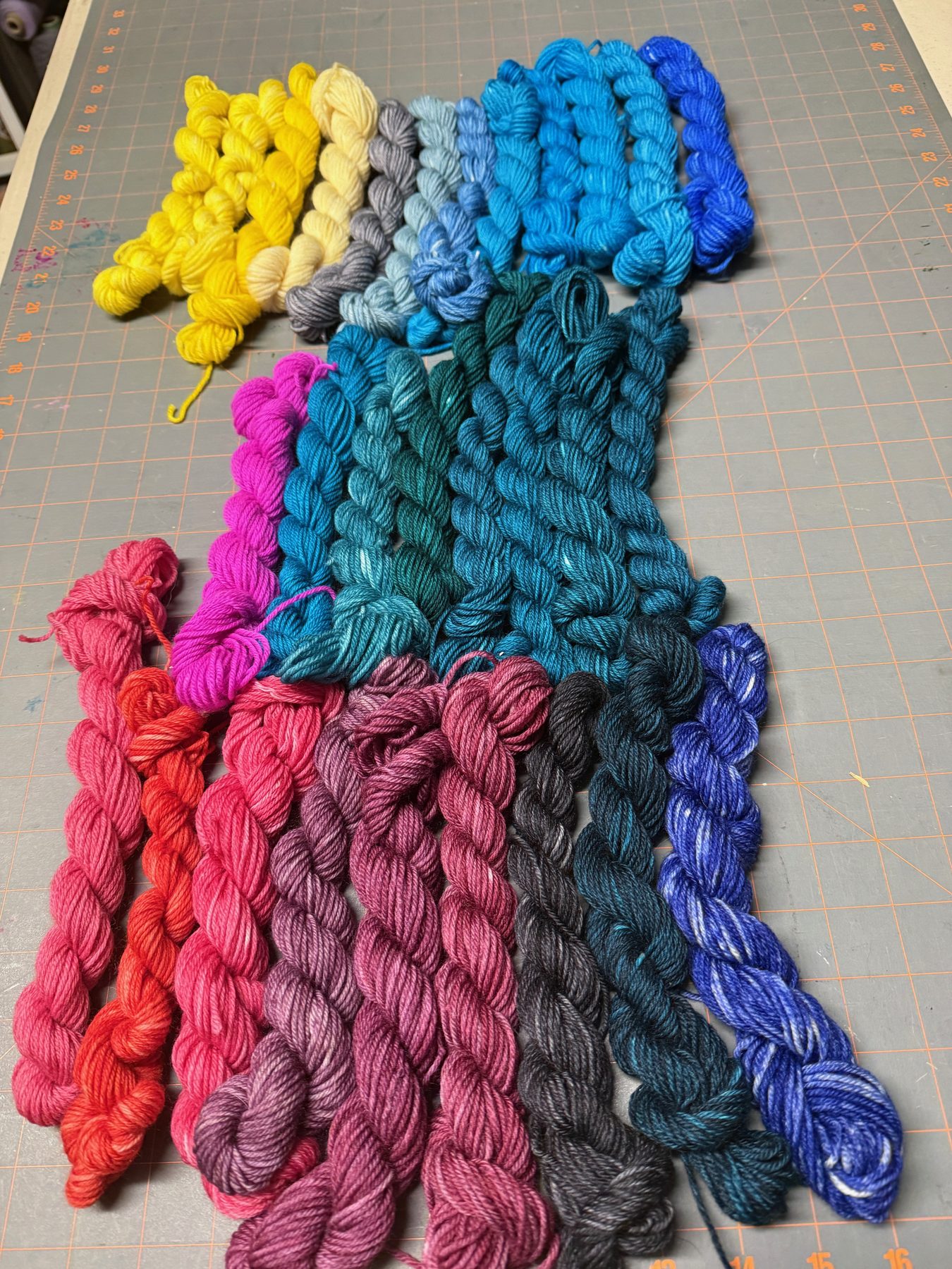 Rainbow of Carol's hand-dyed mini yarn skeins laid out by color